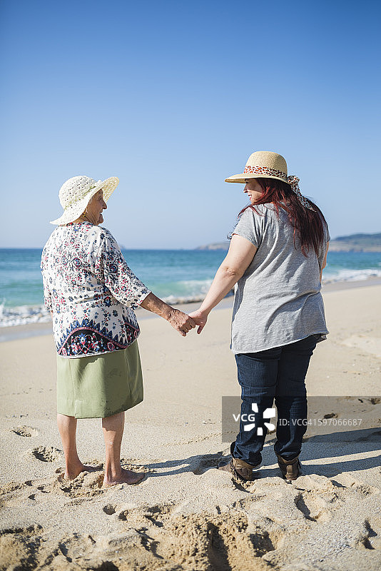 在一个阳光明媚的日子，祖母和成年的孙女在海滩上牵着手图片素材