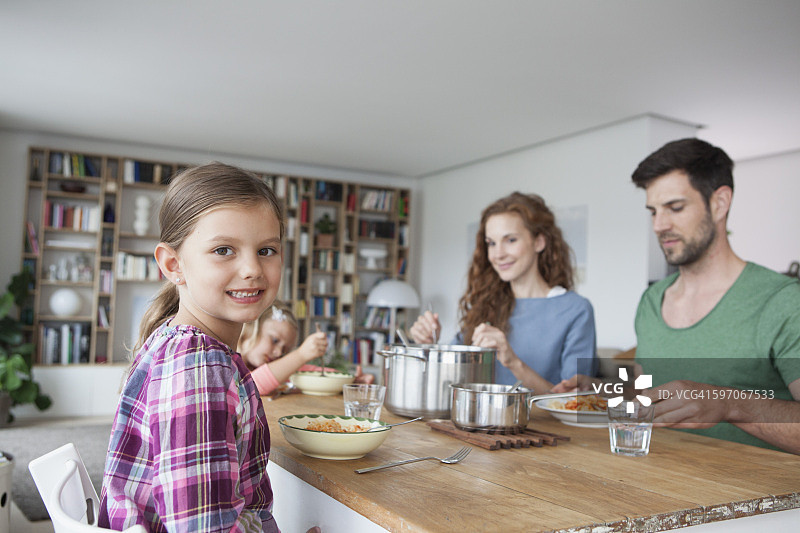 小女孩和她的父母和妹妹坐在餐桌旁的肖像图片素材