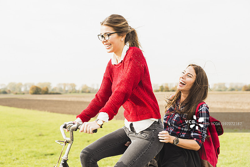 两个快乐的年轻女子在乡村风景中共享自行车图片素材