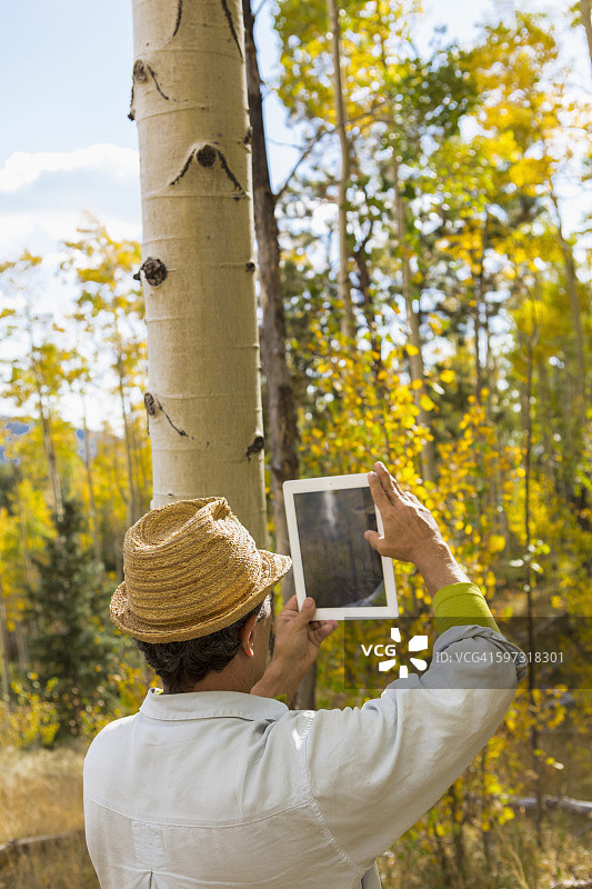 一个人在秋天的森林里用平板电脑拍照图片素材