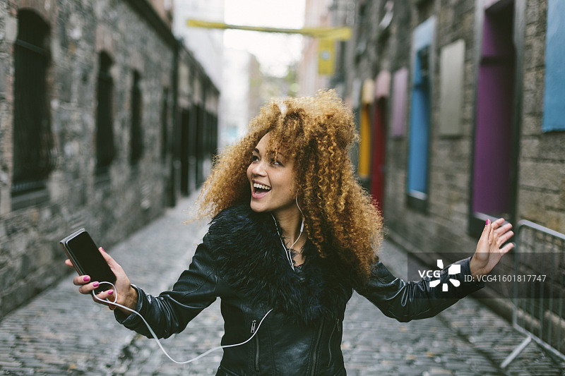 爱尔兰，都柏林，快乐的女人，留着爆炸头，用智能手机和耳机听音乐图片素材