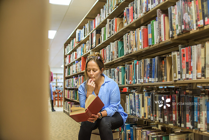 成熟的女人从图书馆的书架上看书图片素材