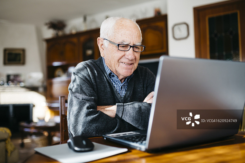 微笑的老人在家里用笔记本电脑的肖像图片素材