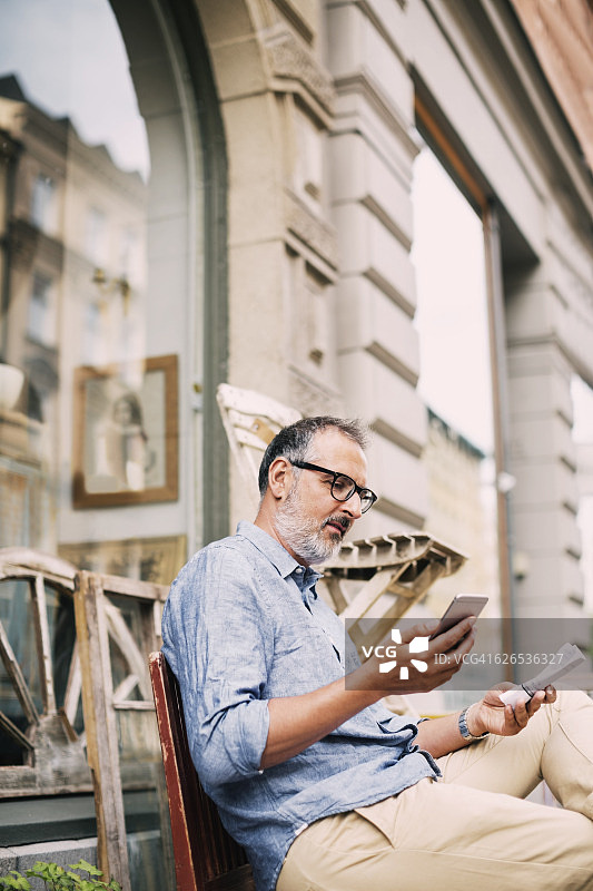 一名男子坐在商店外使用手机图片素材