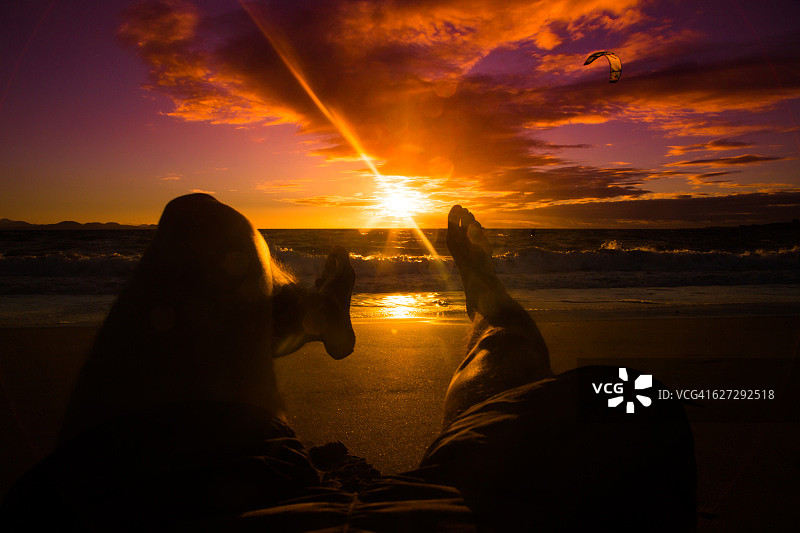 盖伊躺在兰萨罗特岛的海滩上，从个人的角度看，脚和腿在大海和日落。图片素材