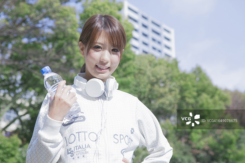 一个日本女人用一个塑料瓶在公园里拿着耳机图片素材