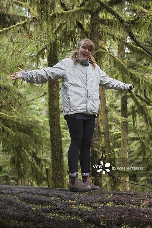 一位年轻女子站在森林中的一根圆木上，双臂伸展着图片素材