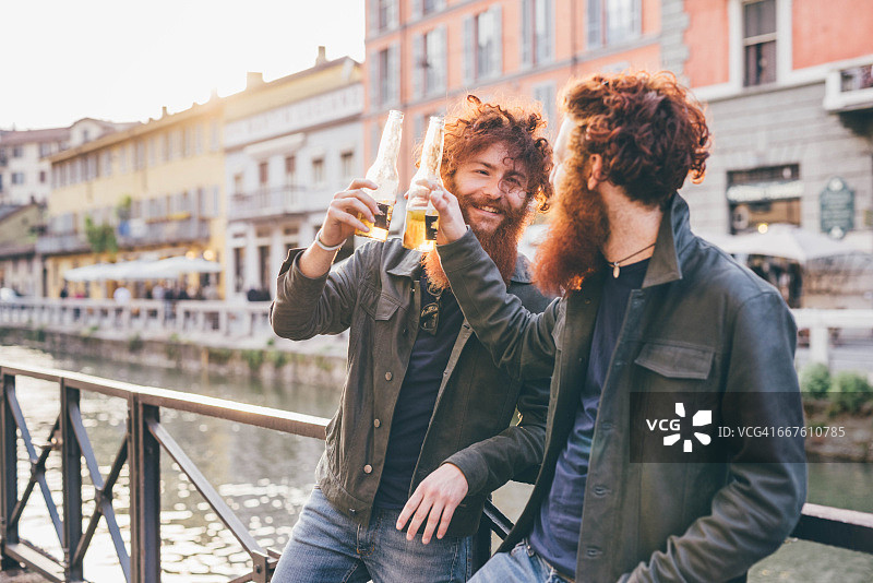 留着红头发和胡子的年轻潮男双胞胎在运河岸边祝酒图片素材