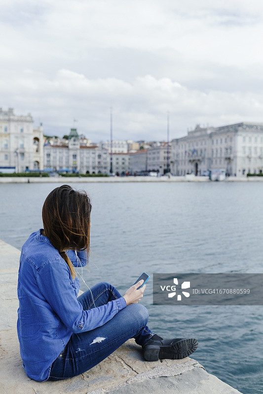 意大利的里雅斯特，一个年轻女子坐在码头上听音乐图片素材