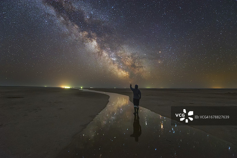 一个男人走在夜晚的盐河上，银河下的星星倒映在河里，俄罗斯。图片素材