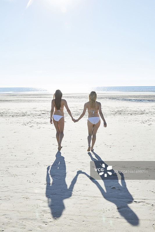 两个穿着比基尼的女性朋友在海滩上手拉手散步图片素材