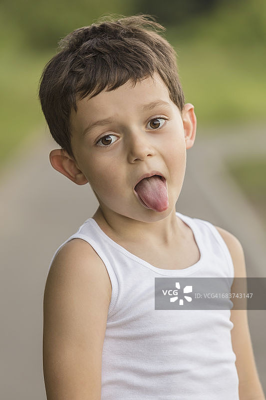 一个男孩站在公园里吐舌头的照片图片素材