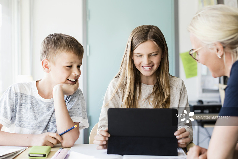 快乐的女孩在用平板电脑，而老师和男孩在教室里看图片素材