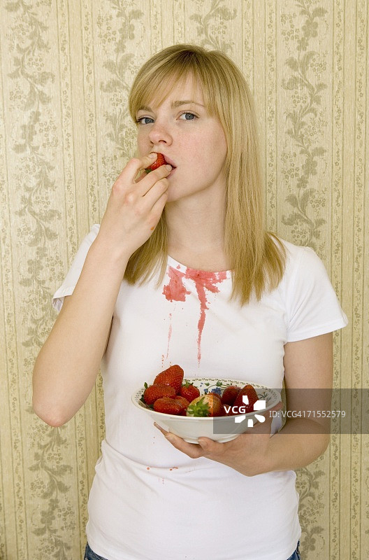 年轻女子吃草莓时把果汁洒在了t恤上图片素材