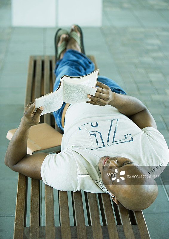 男同学躺在长凳上看书图片素材