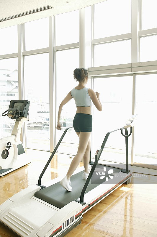 一名年轻女子在设备齐全的健身房锻炼，她在步行者上慢跑图片素材