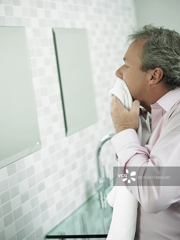 一个成熟男人在镜子前用毛巾擦脸的侧面照片图片素材