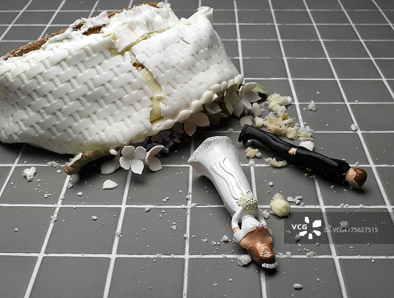 新娘和新郎的雕像躺在被毁的婚礼蛋糕上，铺在瓷砖地板上图片素材