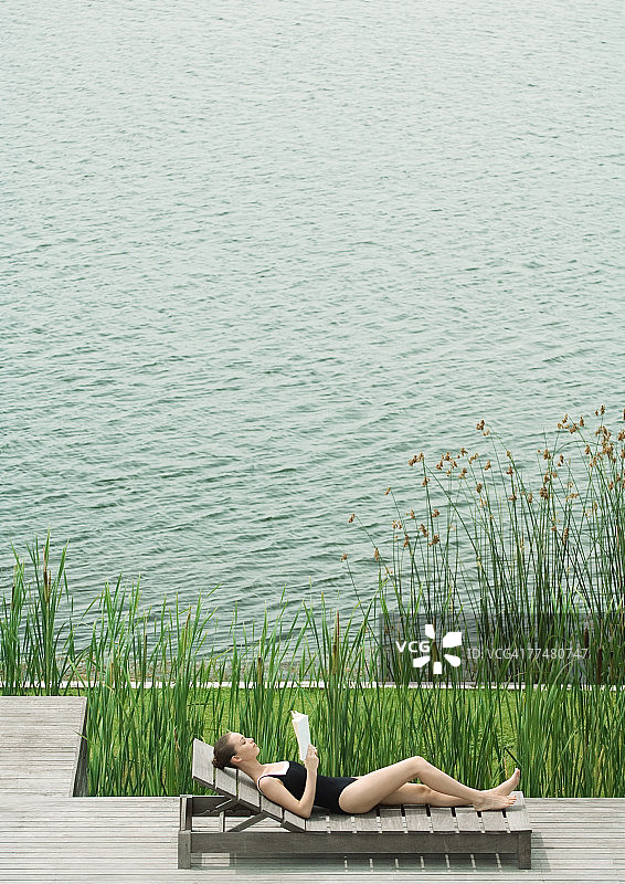 一个女人斜倚在躺椅上，在湖边看书图片素材