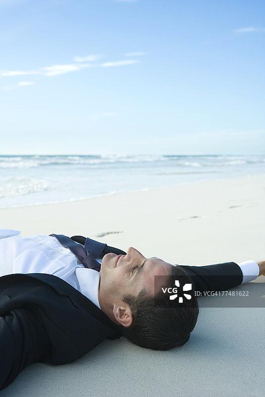 商人躺在沙地上，闭着眼睛，微笑着图片素材