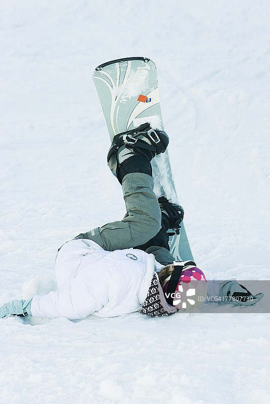 年轻的单板滑雪运动员躺在地上，双腿悬在空中，全身伸展图片素材