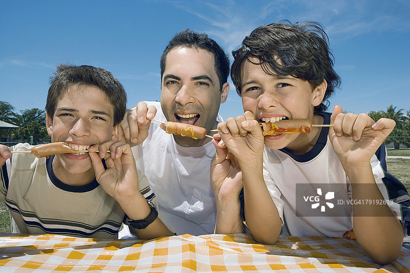 一个中年男人和他的两个儿子在野餐吃香肠的肖像图片素材