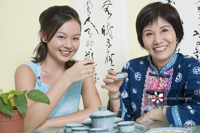一位年长妇女和她的孙女坐在一张桌子旁，拿着茶杯的肖像图片素材