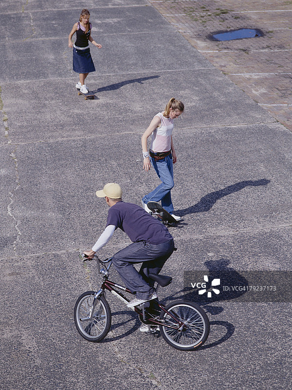 年轻人骑自行车，年轻女子玩滑板图片素材