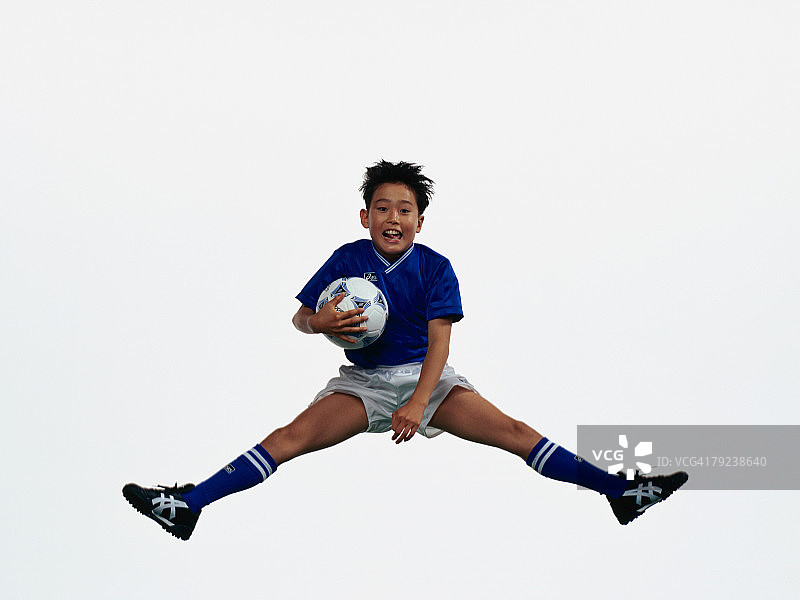 年轻的亚洲男孩拿着足球，在半空中跳跃图片素材