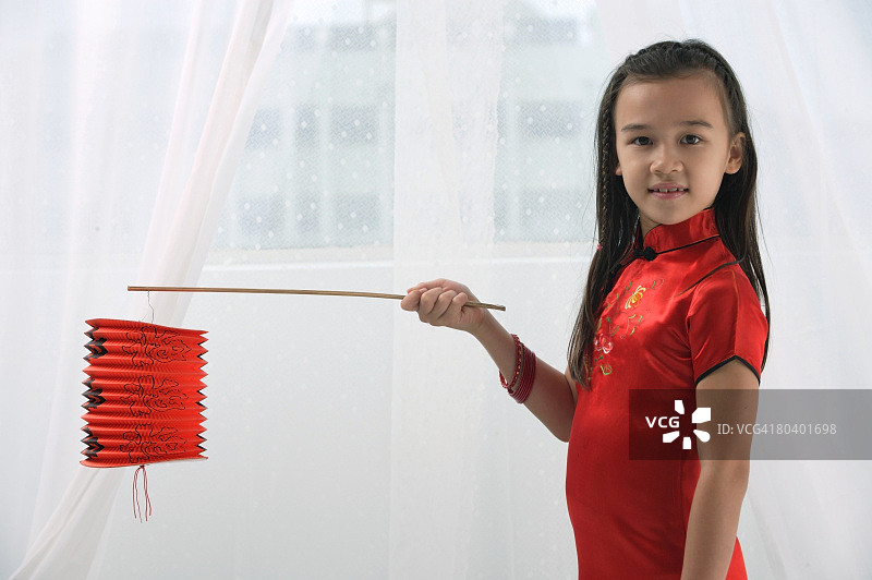 年轻的女孩穿着传统的中国服装，拿着红灯笼，看着镜头图片素材