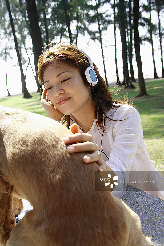 一个年轻女子戴着耳机抚摸着一只狗的特写图片素材