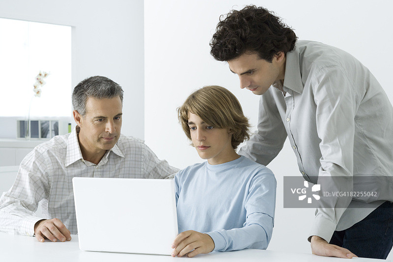 十几岁的男孩与父亲和哥哥一起看笔记本电脑图片素材