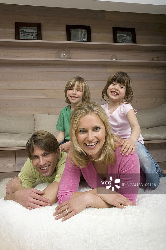 一家人在客厅里，孩子(6-9岁)坐在父母的背上，面带微笑，画像图片素材