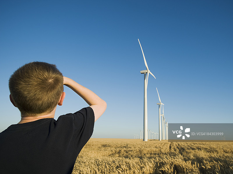 男孩抬头看着风电场里的风车图片素材