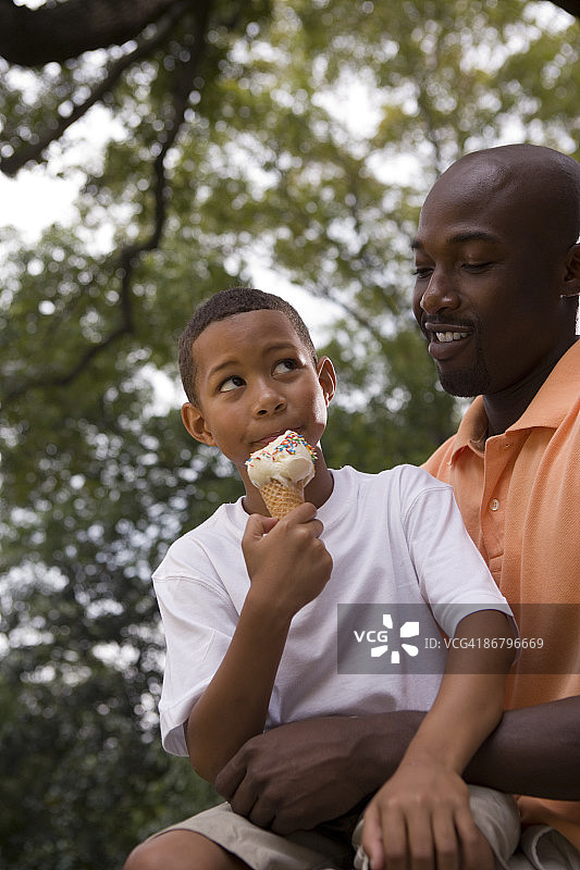 儿子吃着甜筒冰淇淋，坐在父亲的腿上图片素材