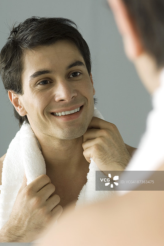 男人在镜子里看着自己，微笑着，肩膀上拿着毛巾图片素材