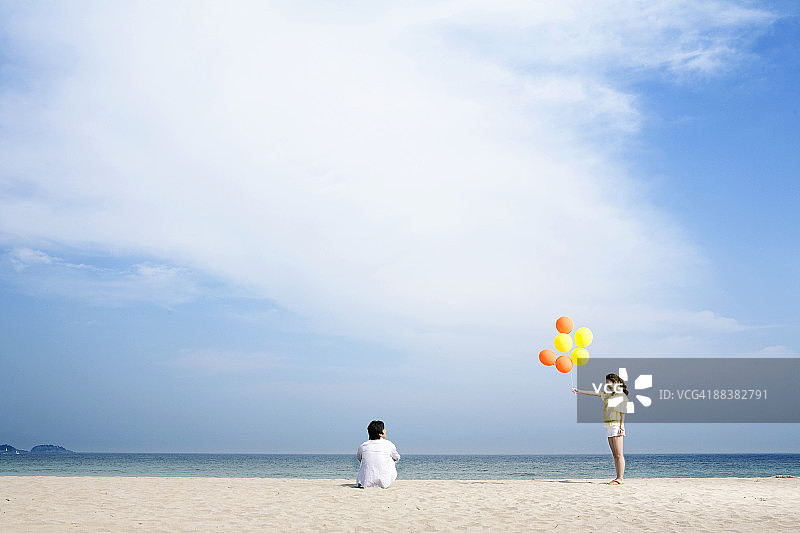 在海滩上，女人把气球递给男人。图片素材