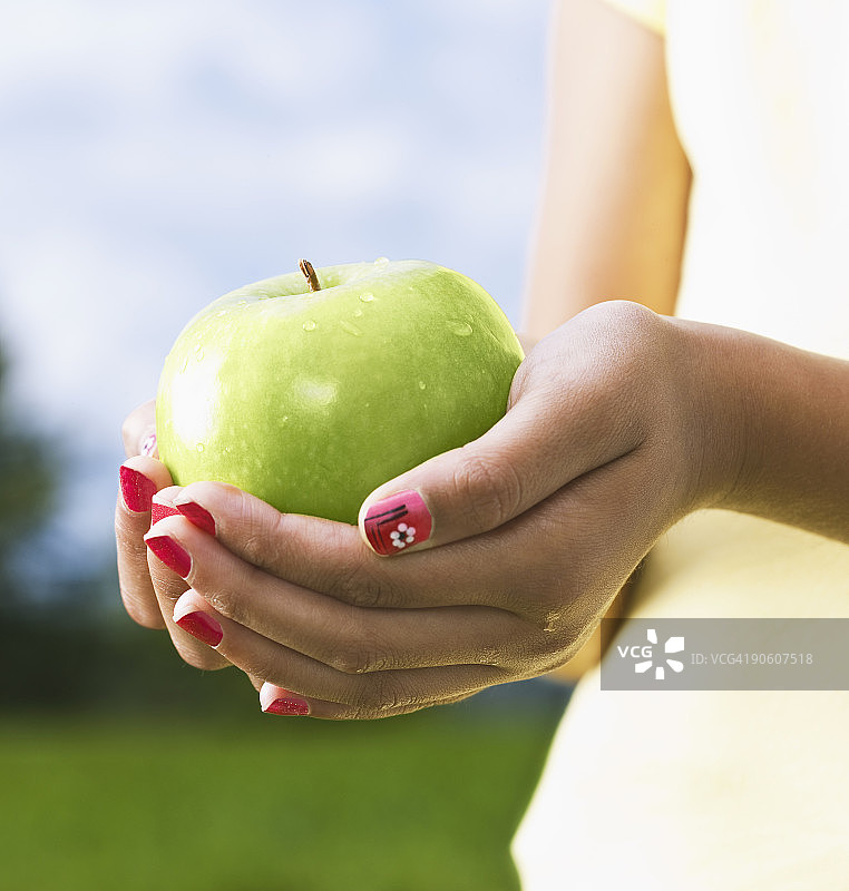 年轻的女孩拿着一个新鲜采摘的青苹果。图片素材