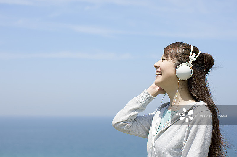 一名年轻女子正戴着耳机在海边听音乐图片素材