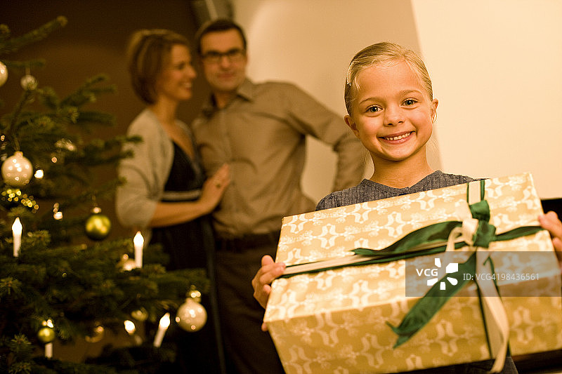 小女孩和圣诞礼物的父母在背后看着图片素材