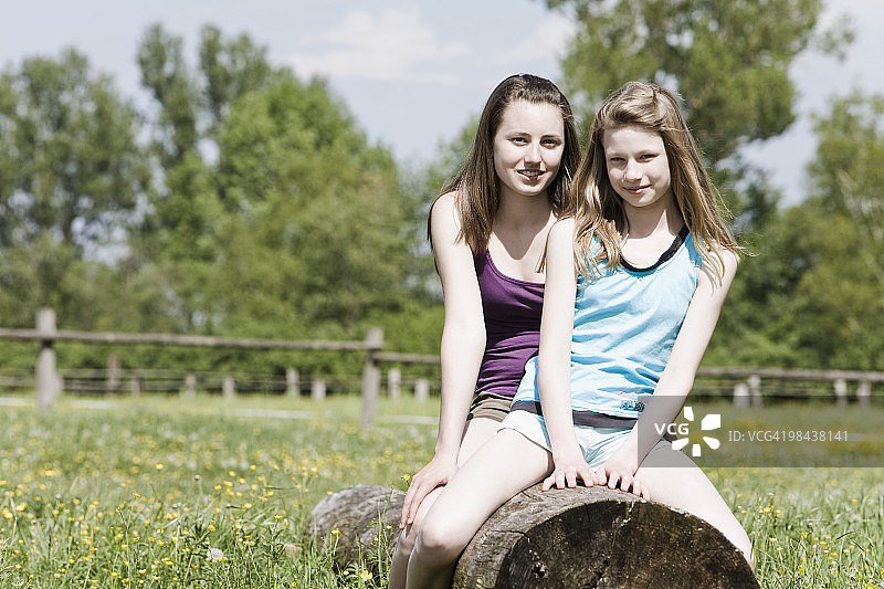 两个女孩一起坐在树干上的肖像图片素材