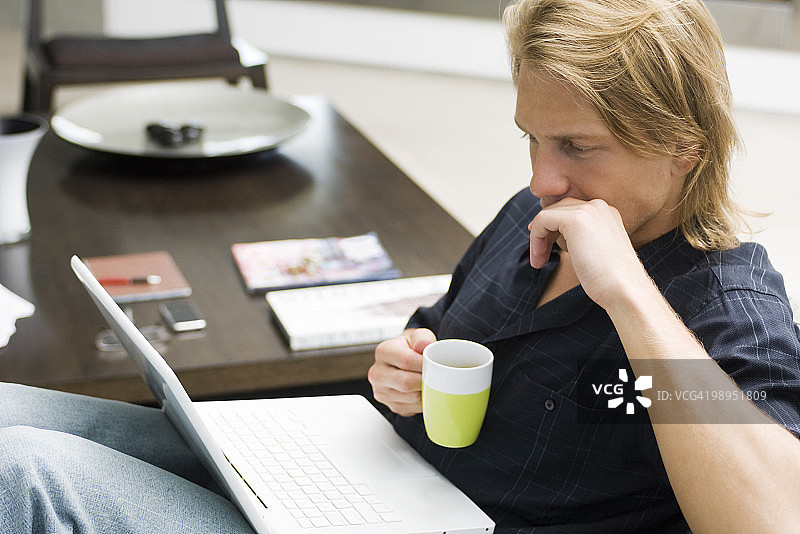 一个男人坐在沙发上，拿着笔记本电脑和一杯咖啡图片素材