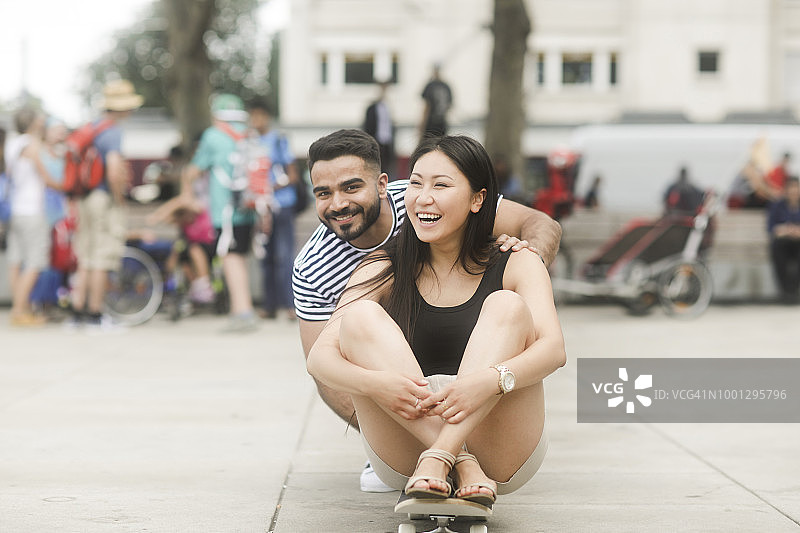 一对微笑的夫妇坐在城市广场的滑板上图片素材