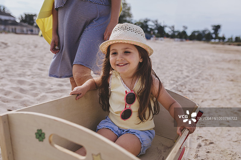 可爱的微笑的孩子坐在一个木车旁边的海滩上她的母亲图片素材