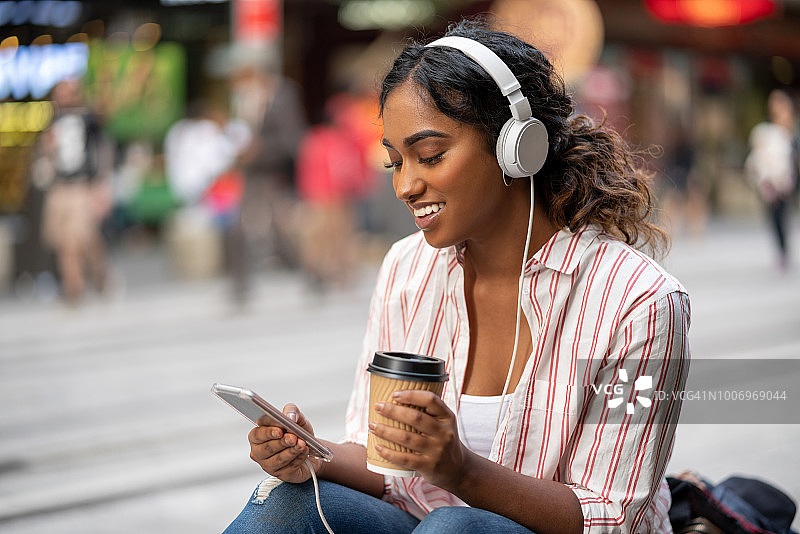 女人在户外戴着耳机听音乐喝咖啡图片素材
