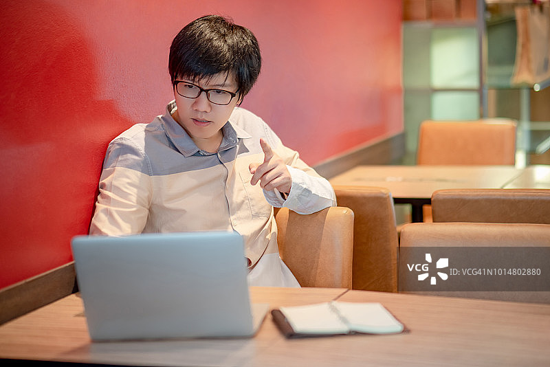 年轻的亚洲人戴着眼镜指着他的手在大学使用笔记本电脑。男大学生在做研究和自学。教育和技术理念图片素材