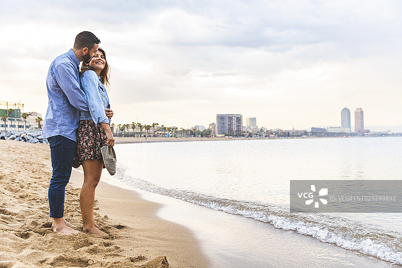 西班牙，巴塞罗那，一对夫妇赤脚站在沙滩上图片素材