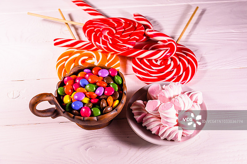 瓷碗，木桌上放着彩色糖果、棒棒糖和棉花糖图片素材