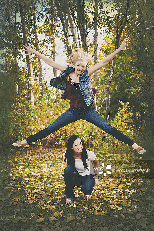 在秋天的公园里，一个年轻女子在她朋友的头顶上跳得很高图片素材