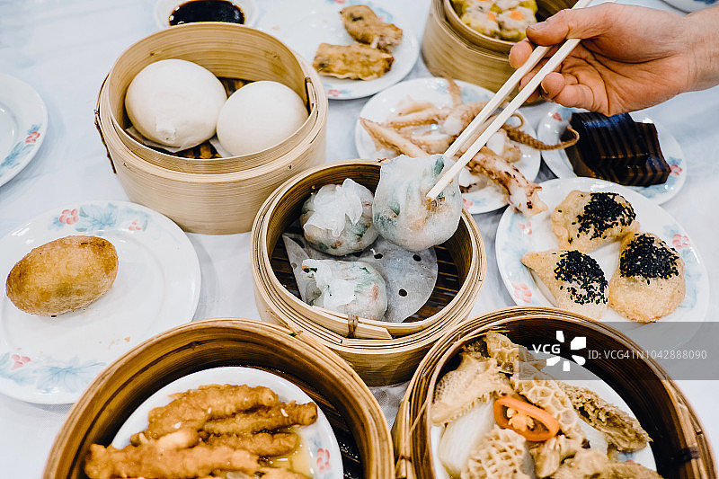 近距离的人的手拿起蒸饺与筷子，享受各种传统点心在中国餐厅图片素材